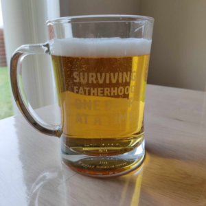 Øl krus med teksten: Surviving fatherhood one beer at a time